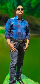 Man in sunglasses standing by a vibrant green lake.