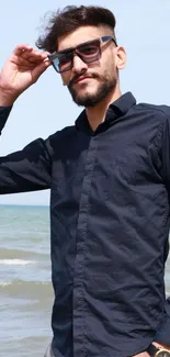 Man in navy shirt and sunglasses by the beach.