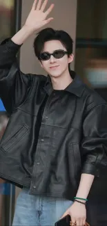 Cool guy wearing black jacket and sunglasses, waving and smiling.