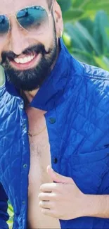 Man in a blue jacket smiling with a green leafy background.