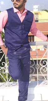 Man in royal blue suit and pink shirt on sunny terrace.