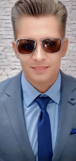 Man in a blue suit with sunglasses against a brick wall.