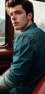 Man in denim jacket sitting in a car with mountains outside.