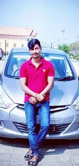 Man in red shirt leaning on a grey car.