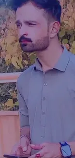 A stylish man in a gray shirt with a nature background.