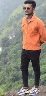 Man in orange shirt standing on a hill with greenery.