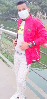 Man posing in red jacket and face mask on urban bridge.