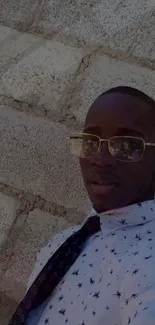 Man in sunglasses posing by a brick wall.