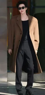 A stylish man in a brown coat and sunglasses, standing with confidence.