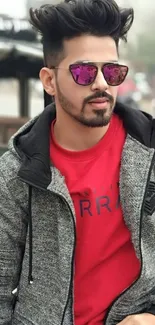 Man in gray jacket and red shirt with sunglasses, urban background.