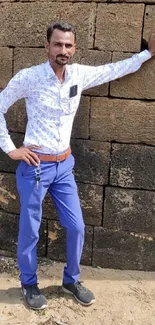 Man in stylish outfit leaning against a brick wall.