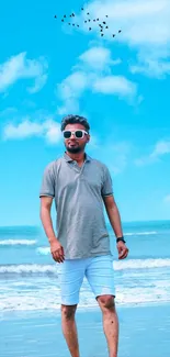 Man in stylish attire walking on a beach under a clear sky.