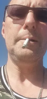 Man with sunglasses and cigarette against blue sky.