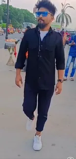 Man in stylish black outfit walking outdoors with confidence.