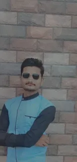 Man in sunglasses with brick wall backdrop, showcasing urban style.