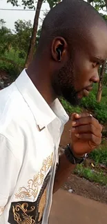 Man with earbuds in park, wearing a designer shirt.