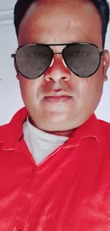 Man wearing sunglasses with a red shirt against a light background.