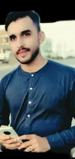 Man in dark blue shirt holding smartphone in urban setting.