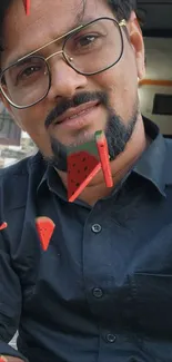 Stylish man with glasses and watermelon art pieces in black shirt.