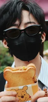 Stylish man wearing sunglasses and mask holds bear-shaped snack.