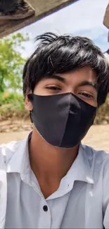 Person wearing a black mask outdoors, in natural light.