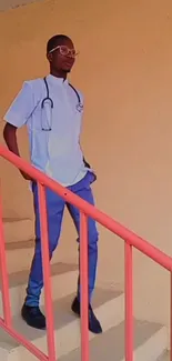 Medical professional in blue scrubs on staircase with light orange background.