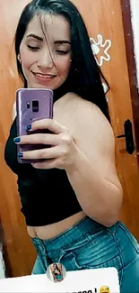 Woman taking mirror selfie with purple phone, wearing casual outfit.