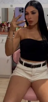 Woman taking a mirror selfie wearing a black top and white shorts.