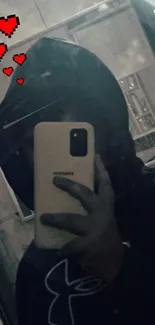 Hooded figure taking selfie with pixel hearts in mirror.