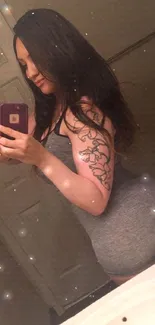 Stylish woman with tattoo takes a mirror selfie, showcasing her chic outfit.