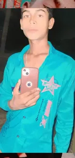 Mirror selfie in teal shirt holding a smartphone.