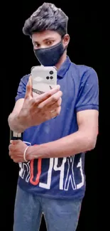 Young man in blue shirt taking a selfie against black background.