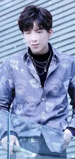 Stylish young person in patterned blue shirt against modern backdrop.