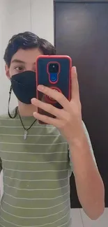 Person taking a mirror selfie with a phone wearing a mask and striped shirt.