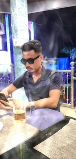 A person with sunglasses using phone at a stylish café on a dark night.