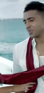 Man in stylish attire with ocean backdrop and red scarf.