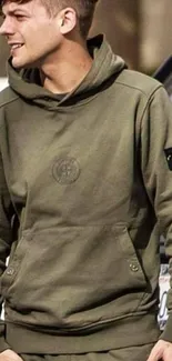 Person wearing olive green hoodie with emblem, casual fashion.