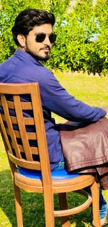 Man in sunglasses sitting on a wooden chair outdoors.