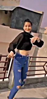 Woman dancing on rooftop wearing casual jeans and black top against a clear sky.