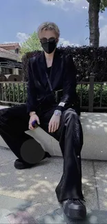 Trendy person in black attire sitting outdoors.