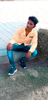 Young man in casual wear sitting outdoors against greenery.