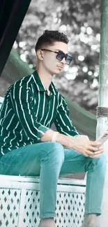 Person in green-striped shirt sitting outdoors with smartphone.