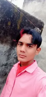 Young man in pink shirt against a weathered concrete wall.