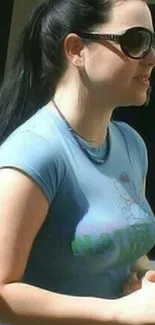 Woman in sunglasses and blue shirt outdoors.