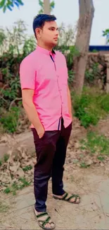 Person in pink shirt standing outdoors, surrounded by greenery.