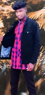 Young man posing in stylish outfit outdoors with leafy background.