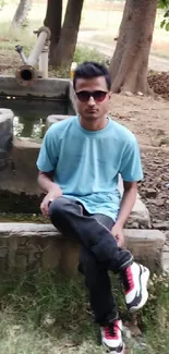 Young person in blue shirt outdoors, seated near rustic setting.