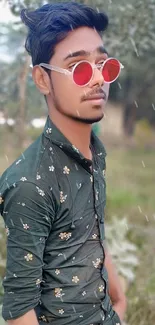 Person in floral shirt and red sunglasses posing outdoors.