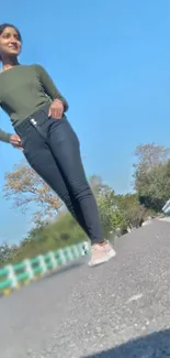 Woman in stylish outfit standing on a road with a blue sky backdrop.