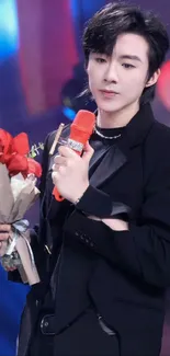 Stylish performer in black holding a bouquet on stage.